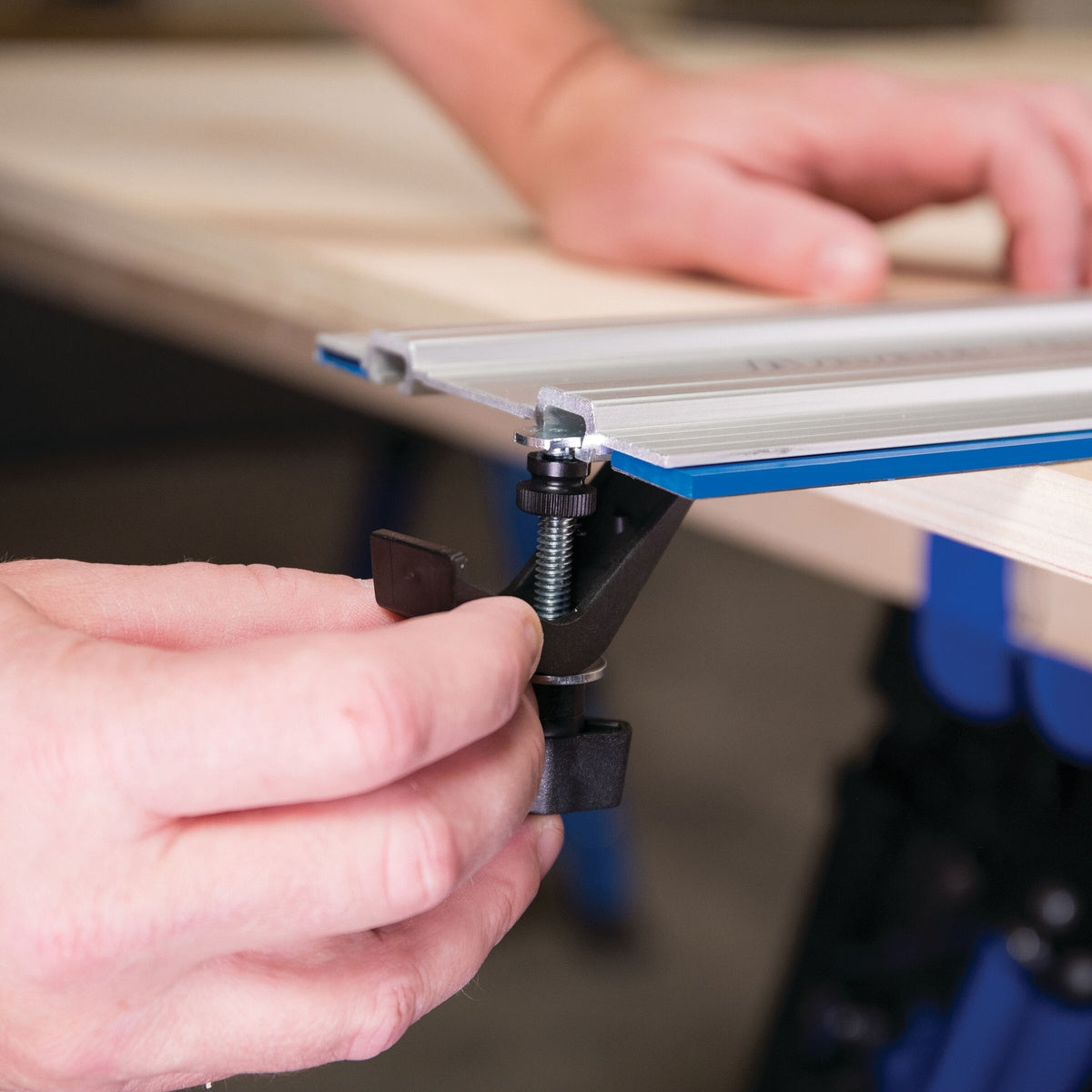 Kreg KMS7520 Track Clamps securing a Kreg guide track to a wood panel during circular saw cutting setup on a workbench