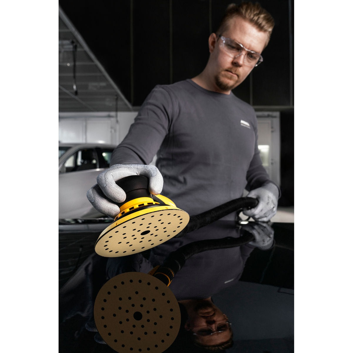 Mirka orbital sander with Gold Multifit sanding disc on a glossy automotive panel