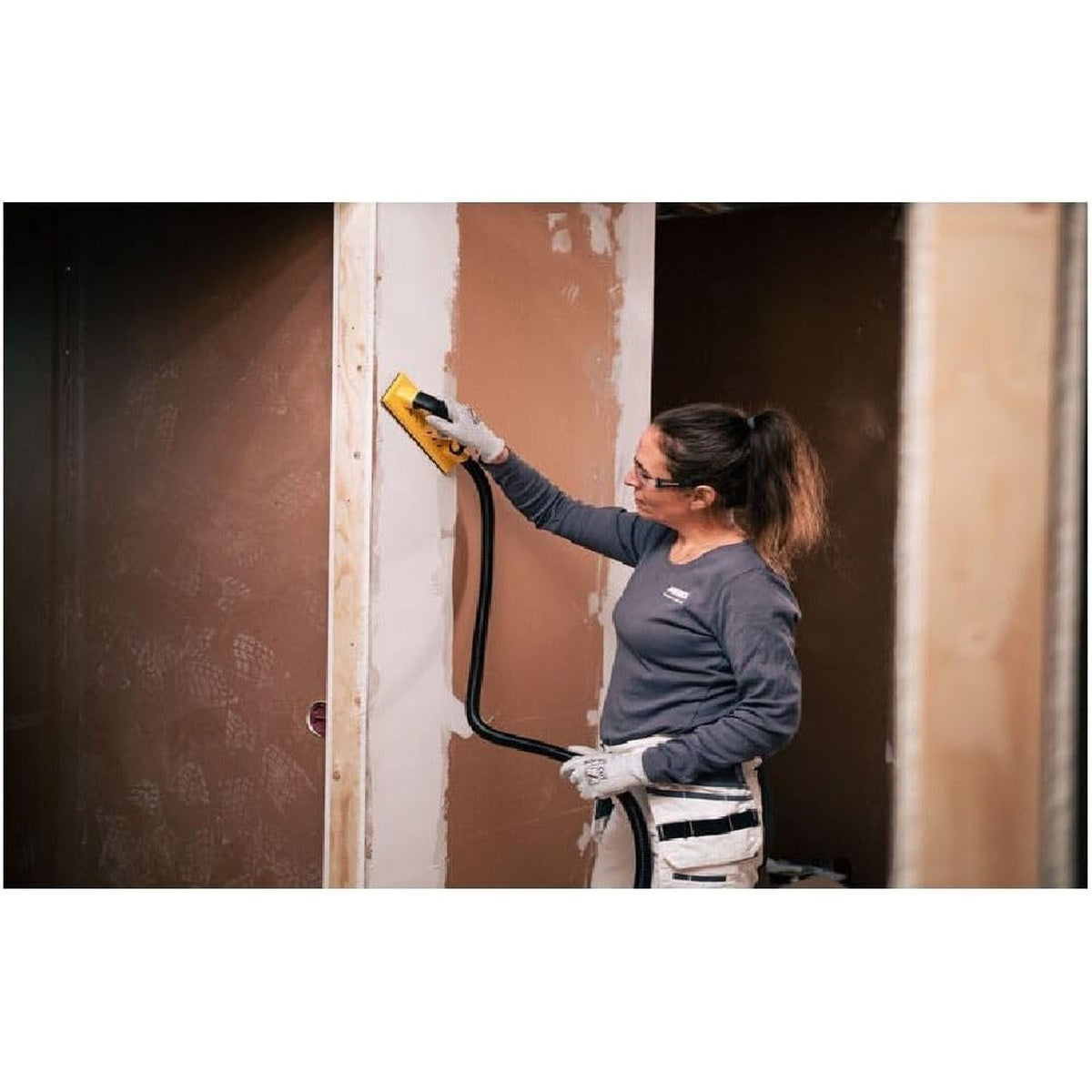 Worker using Mirka sanding setup on drywall surface