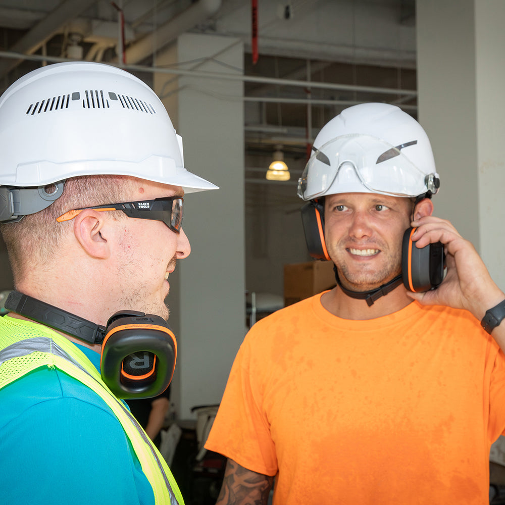 Klein Bluetooth Behind-the-Head Earmuffs worn under a hard hat on a jobsite