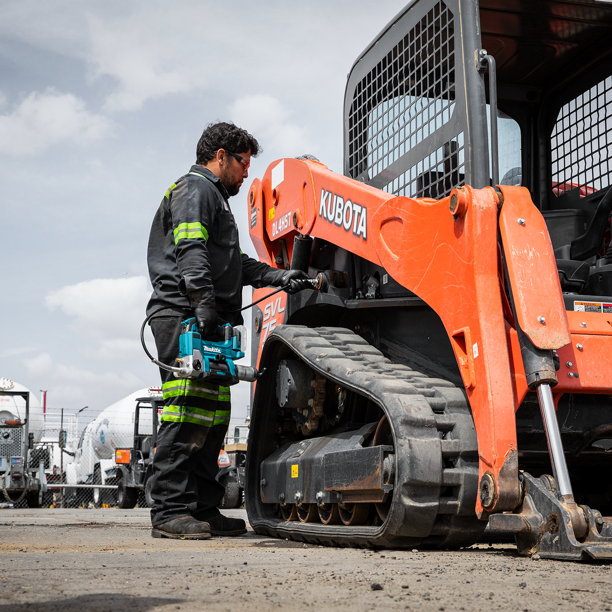 Technician using the Makita 18V LXT cordless grease gun on a compact track loader at a jobsite