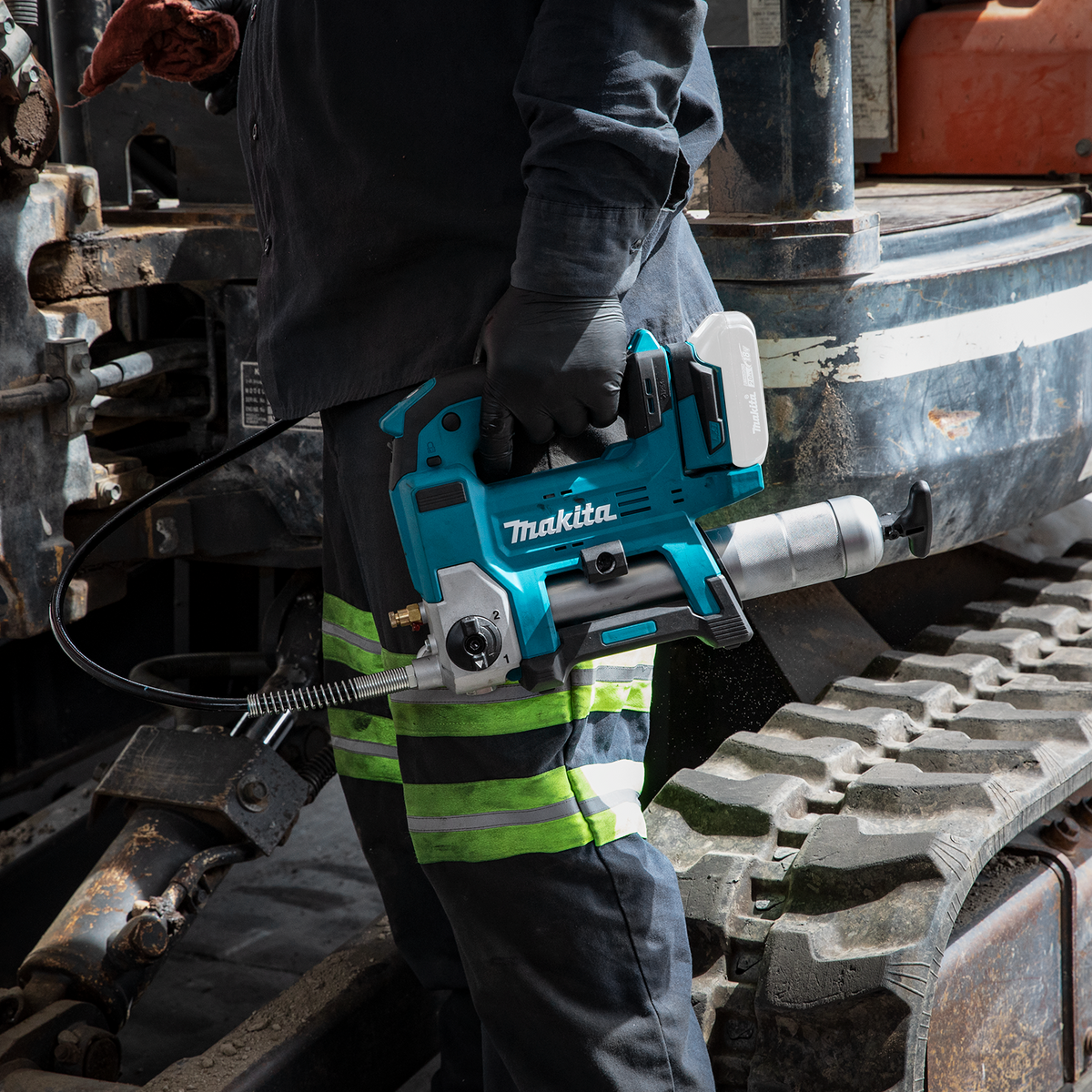 Makita 18V LXT cordless grease gun hose connected to a fitting on a tracked machine undercarriage