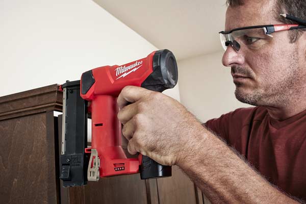 Man using Milwaukee 2540 23 Gauge Pin Nailer on a cabinet wearing PPE